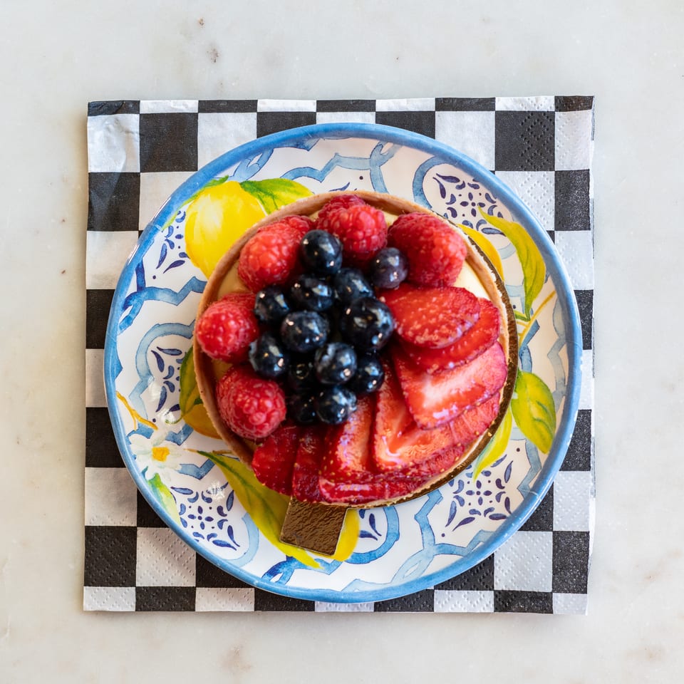 A vibrant fruit tart with strawberries, blueberries, and raspberries on a decorative plate.
