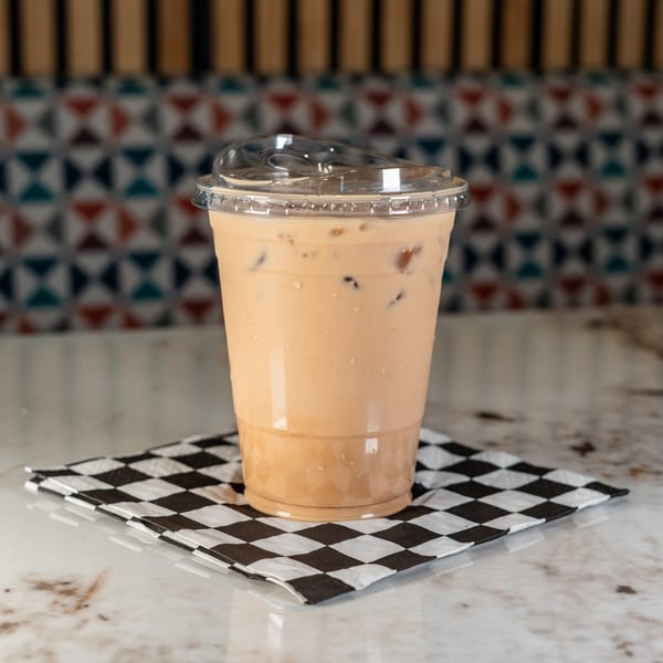 Iced coffee in a plastic cup with a lid, on a black and white checkered napkin.