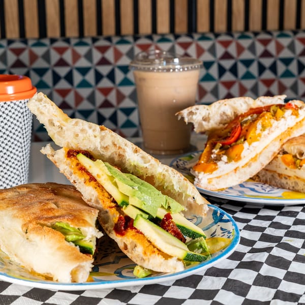 Two focaccia sandwiches, one with zucchini and avocado, the other with roasted peppers and cheese.